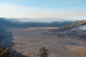 Volcanic landscape featuring a vast plain hills and a mountain range under a clear sky
