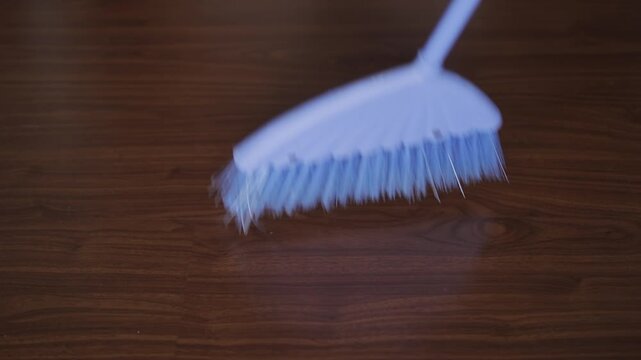Broom with synthetic bristles sweeping dust and debris from a wooden laminate floor. Housekeeping and domestic chores concept