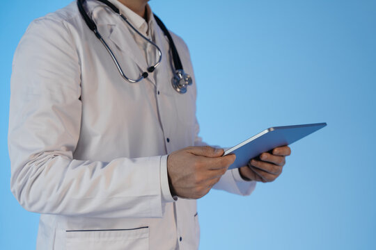 Doctor holding tablet device for teleconsultation and AI-assisted healthcare system concept on blue background, representing future technology in medicine. - Powered by Adobe
