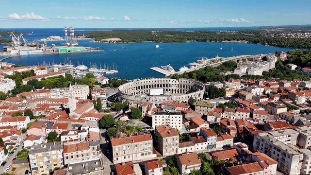 Excellent top-down aerial view of an ancient town and large amphitheater on a sunny day with a bright sea harbor in the background
