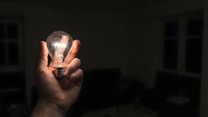 Person Holding Bright Light Bulb in Dark Room.