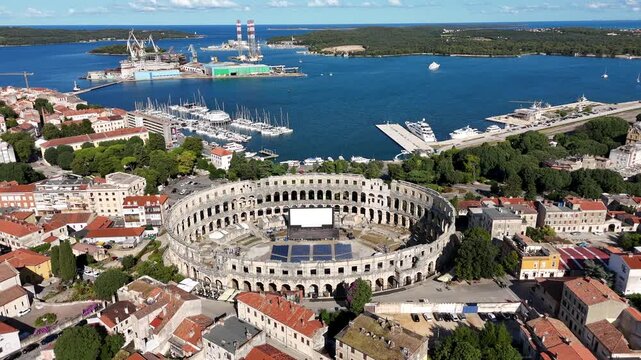 Smooth orbital drone shot around an ancient Croatian amphitheater in Pula on a clear sunny day with the surrounding historic town visible