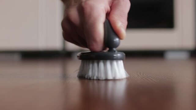 Close-up of a janitor's hand scrubbing a dirty wooden surface. Housekeeping and cleaning service performing deep cleaning duties in a home