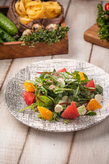 Fresh green salad with watermelon orange segments and creamy dressing served on a patterned plate