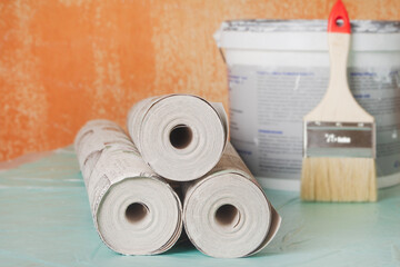 Wallpaper rolls, a brush, and paint against an old wall in a house or apartment. Renovation preparation concept