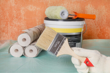 A handyman holds a brush against a backdrop of building materials. Wallpapering and painting a dilapidated room. Renovation concept