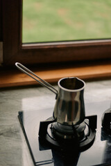 Closeup of a small saucepan resting on a gas burner in a kitchen, metal surface reflecting light, portraying a simple home cooking scene