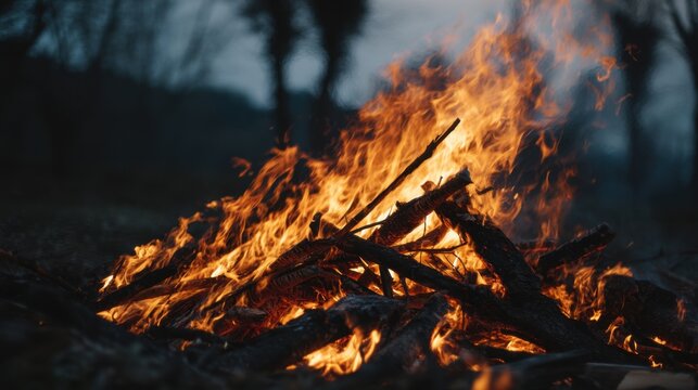 A pile of wood with a lot of fire on it. The fire is orange and yellow. The fire is very large and is in the middle of the pile of wood