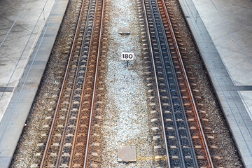 Fototapeta premium Symmetrical rail tracks at platform edge with markers and gravel between rails