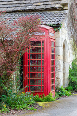Iconic red British telephone booth nestled against a stone wall with ivy, garden wildflowers, and moss
