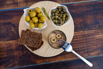 Tuna can next to a bowl of olives and capers