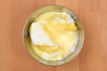 An overhead view shows a stainless steel bowl with snenokle dessert - meringues in vanilla custard - on a wooden background