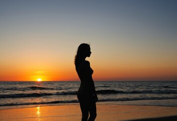 Fototapeta premium Silhouette of a young woman standing on the beach at sunset