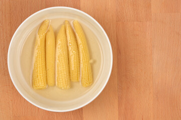 Five canned baby corn pieces in a bowl with liquid on a wooden surface