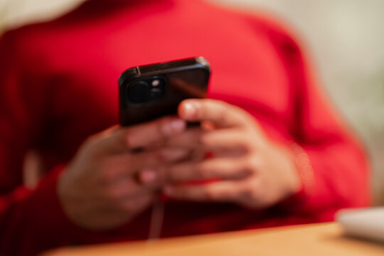 A person in a red sweater uses a smartphone, their hands holding the device as they interact with the screen.