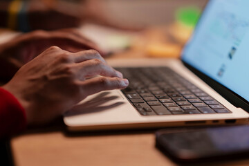A person's hands are typing on a laptop keyboard, with a smartphone resting nearby on a wooden desk.