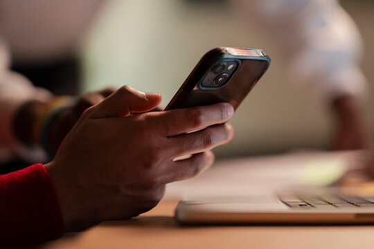 A person's hands are holding a smartphone, with a laptop keyboard in the foreground. The focus is on the device and the user's interaction with it.