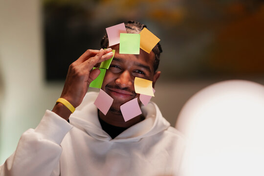 A young man with a playful expression sticks colorful notes to his face, symbolizing brainstorming and creative thinking.