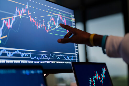 A person's hand points to a financial chart on a computer screen, analyzing market trends and data.