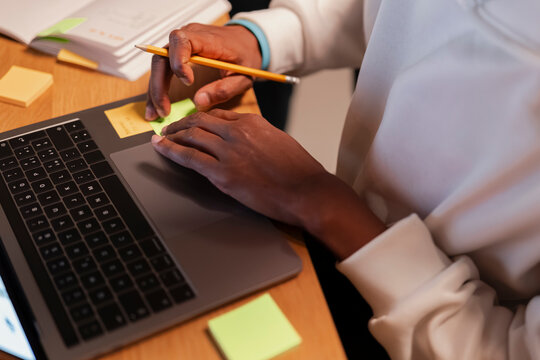 A person's hands are shown working on a laptop, with a pencil and sticky notes on a wooden desk, suggesting productivity and organization.