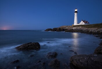Fototapeta premium Lighthouse on the Coastline at Dusk with Rocky Shore
