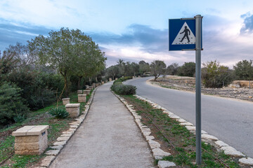 Curving roadway and footpath with a pedestrian crossing sign at Zippori National Park in northern Israel. Quiet evening light, olive trees and cloudy sky create a serene scene