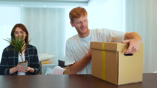 Portrait of happy Caucasian couple unpacking kitchen stuff from cardboard boxes in new apartment. Joyful boyfriend and girlfriend moving in new house. Unpack in new apartment. Family concept