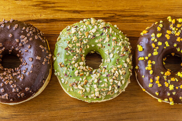 assorted freshly baked donuts with chocolate and nut glaze on wooden surface top view close up