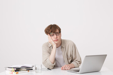 Portrait of sad bored young man student wears beige shirt and spectacles looks tired sitting at the...