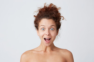 Horizontal shot of surprised pretty young woman with healthy soft skin after applying mask or body cream, curly hair and opened mouth shouting and looks amazed isolated over white wall