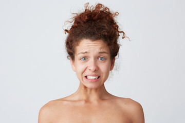 Close up shot of upset worried young woman with curly hair and healthy skin after applying mask or cream feels confused and embarrassed isolated over white background