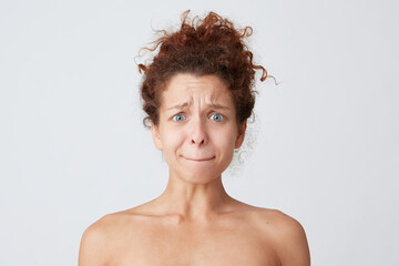 Cropped shot of sad embarrassed young woman with curly hair and healthy skin pressed her lips, feels confused, abused and sad isolated over white background Standing half naked after shower