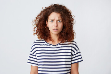 Closeup of angry serious young woman with curly hair wears striped t shirt feels displeased and looks worried isolated over white background