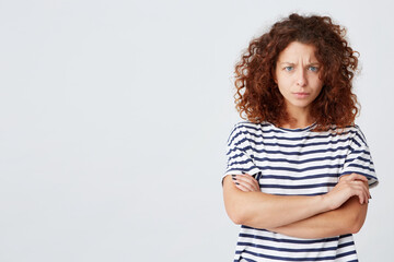 Closeup of angry stressed curly young woman wears striped t shirt have problems and stands with arms crossed isolated over white background