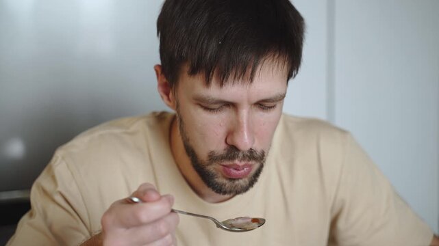 Handheld portrait of man blowing on spoon to cool food before eating. Serving very hot entree poses, risk of scalding and burning the oral mucosa.