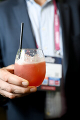 Close-up of a hand holding a stemless glass with a reddish-pink beverage and black straw
