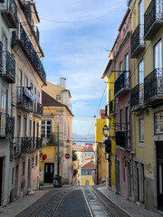 Colorful historic buildings lining a steep street with tram tracks in Lisbon
