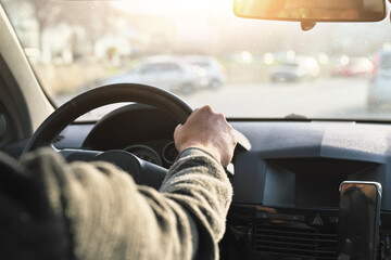 Men&rsquo;s driver's hand holding steering wheel of car while driving.