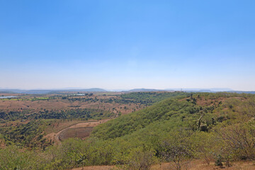 Mhaismal, MH, India, Dec 12: Panoramic view of green, rolling hillsides, valleys, and dry, brown scrub land extending to the hazy horizon under a clear blue sky.