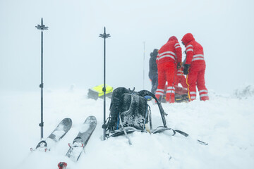 Paramedic team of emergency service helping in mountains in winter during blizzard. Selective focus on ski poles in snow and backpack. Themes rescue in extreme weather.