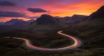 Scenic mountain road with light trails at sunset.