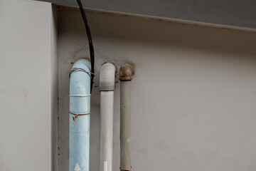 Old plumbing pipes and electrical cables on a concrete wall, showing blue, grey, and rusty textures for industrial infrastructure backgrounds.