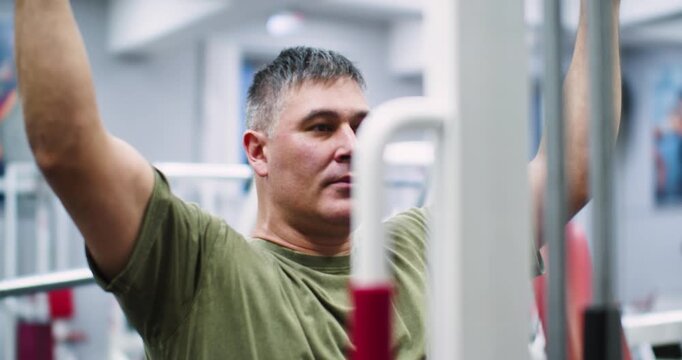 Slow motion cropped 4k footage of a middle aged Caucasian man working out in the gym. Workout for back muscles. Physical education as a norm of life for maintaining health.
