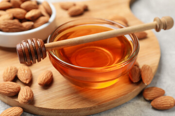 Honey in bowl, almonds and dipper on light grey table, closeup