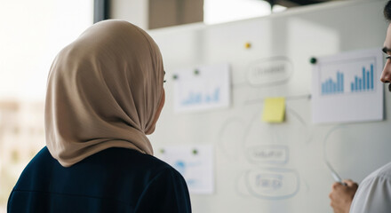 Businesswoman in hijab analyzing charts on whiteboard during meeting