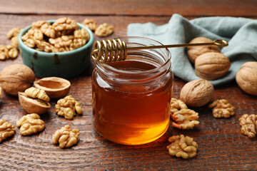 Honey in jar, dipper and walnuts on wooden table, closeup