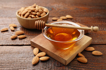 Honey in bowl, dipper and almonds on wooden table, closeup