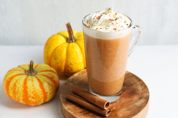Delicious pumpkin latte with whipped cream, cinnamon sticks and fresh vegetables on white table near grey wall, closeup