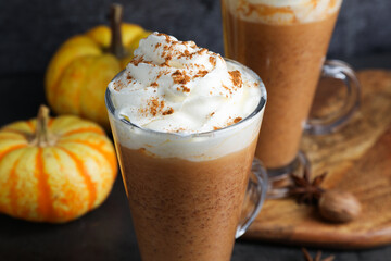 Delicious pumpkin latte with whipped cream, spices and fresh vegetables on dark table, closeup