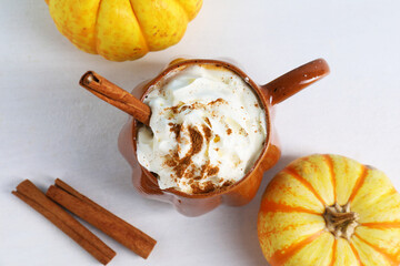 Delicious pumpkin latte with whipped cream in cup, cinnamon sticks and fresh vegetables on light table, flat lay